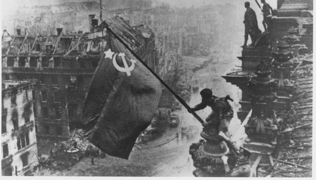 Russian soldiers flying the Red Flag, made from table cloths, over the ruins of the Reichstag in Berlin